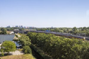 Uitzicht op de Thomas R. Malthusstraat in Amsterdam met een passerende intercitytrein en omliggend groen.